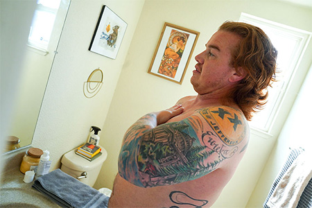 Man with red hair rubs gel into right shoulder in his bathroom.