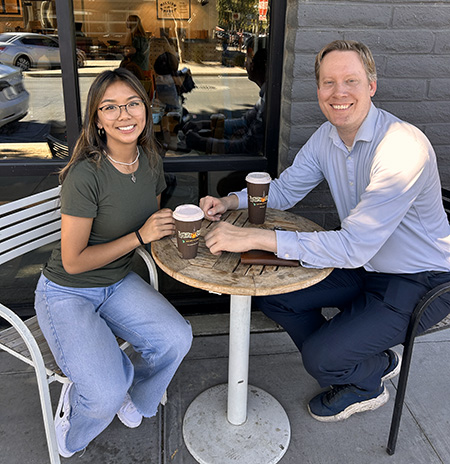 Man and woman sit at an outdoor cafe drinking coffee.