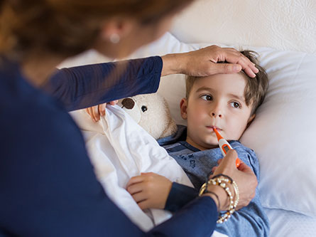 Boy laying in bed getting his temperature taken by his mom